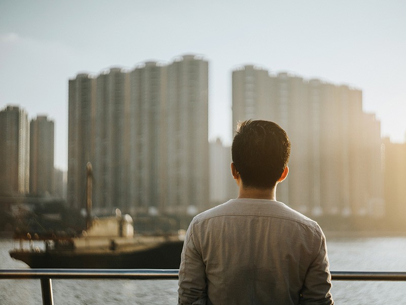 A man standing near the river and looking towards real estate building