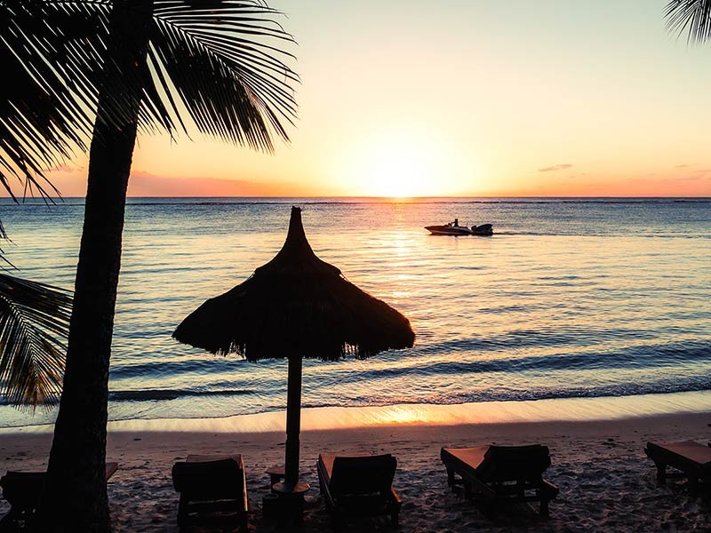 sunset view near a hotel in mauritius and  a ship sailing in the water