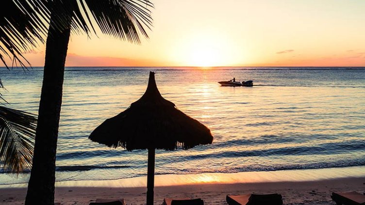 sunset view near a hotel in mauritius and  a ship sailing in the water