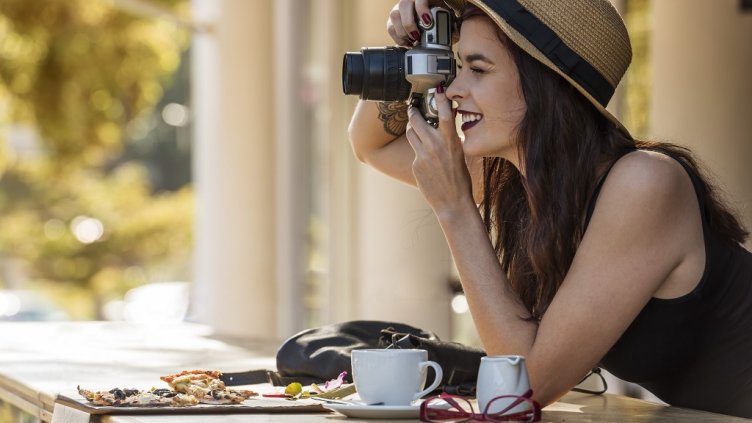 young beautiful traveler happily taking photos with camera at cafe