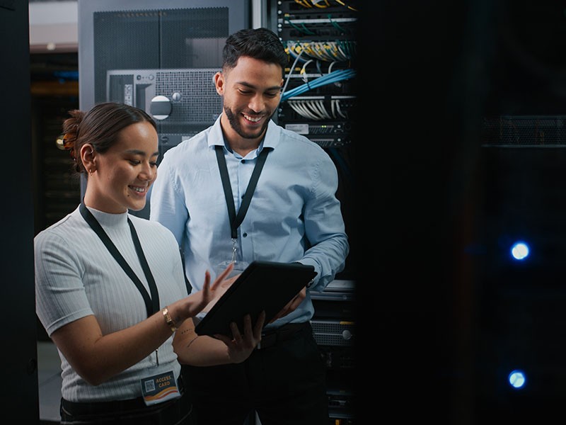 Two employees smiling while looking at the tablet inside data centre