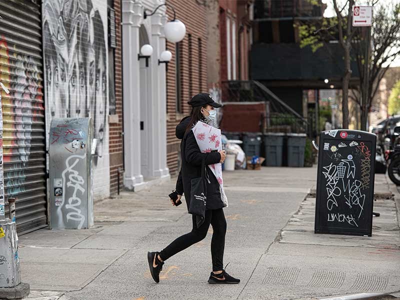 A woman walking on road while wearing a mask and carrying flower bouquet