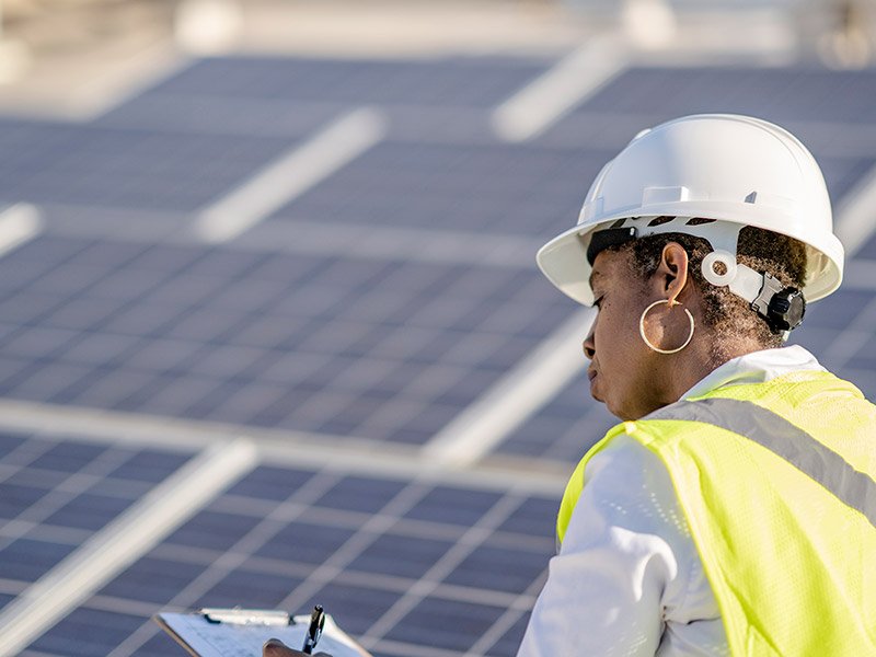 Woman wearing hard hat in front of solar panels