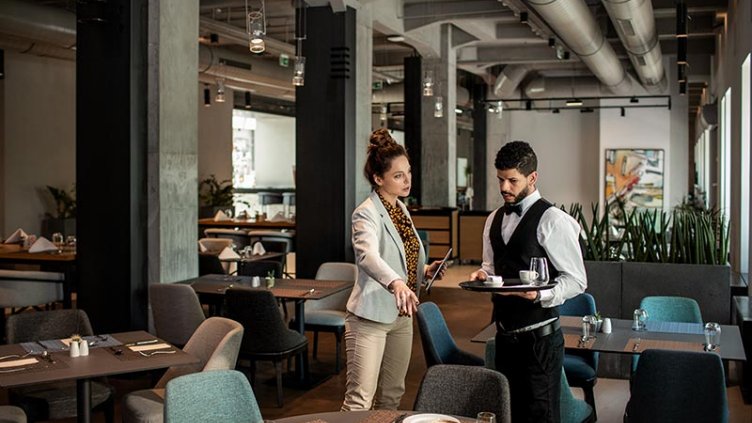 Hotel manager providing guidance to waiter in the restaurant.