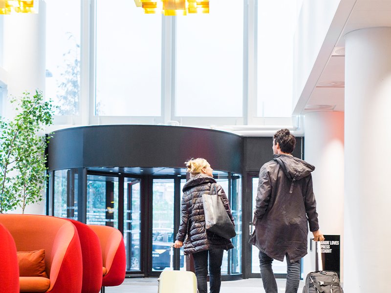 Backside of business professionals walking with luggage in hotel lobby