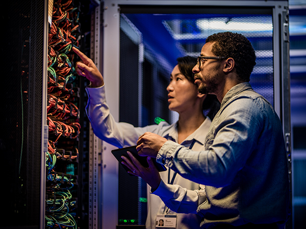 Male and female IT engineers checking servers in server room with help of tablet.